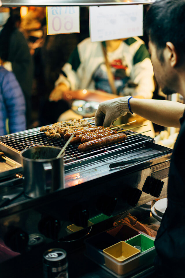 a vendor man barbecuing skewers in a night market